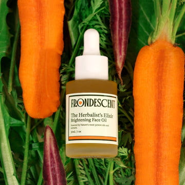 Frondescent's face oil laying on top of dandelion leaves and surrounded by carrots