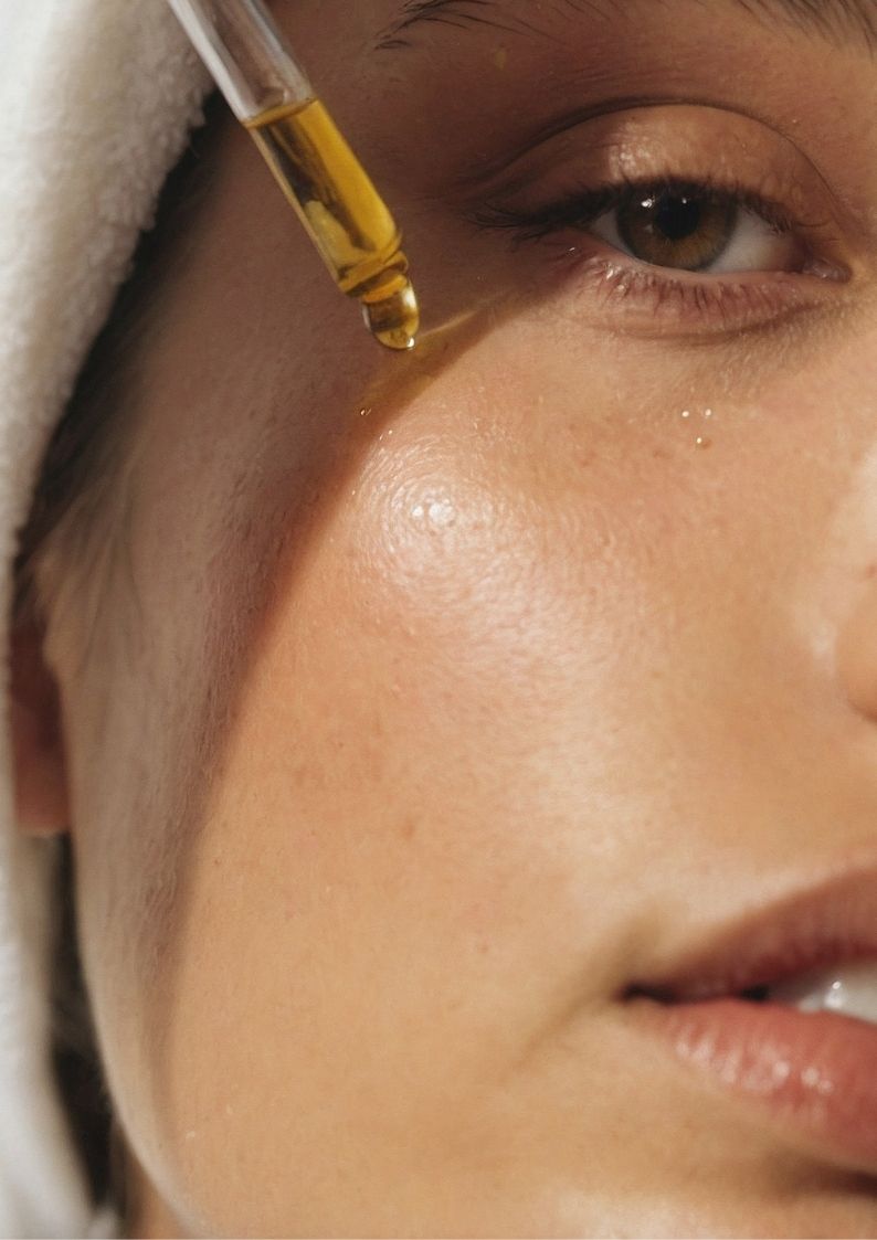 Close-up of a person applying a dropper with yellow liquid to their face.