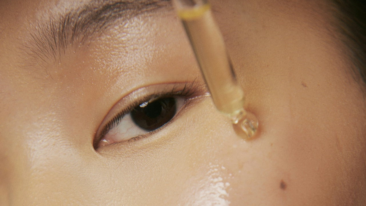 Close-up of face oil applying liquid to the skin near an eye.