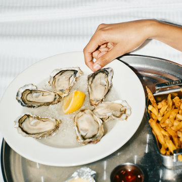 Oysters on a bed of ice with a lemon wedge, served with a side of fries.