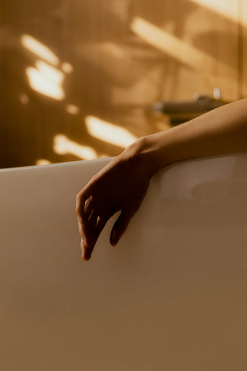 Hand resting on the edge of a bathtub with a warm, blurred background